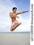 A man in shorts jumping on a beach