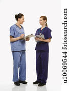 Portrait of Caucasian women doctors in medical scrubs standing talking holding medical charts against white background.