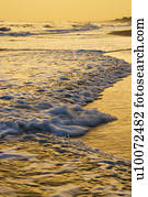 Waves lapping on beach at sunset.