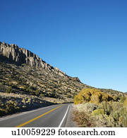 Strip of highway cutting through montain range under clear blue sky.