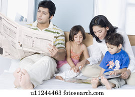 Young woman showing a magazine to her children with her husband reading a newspaper beside them