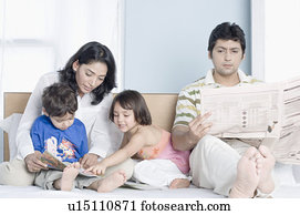 Young woman teaching her children with her husband sitting beside them and reading a newspaper